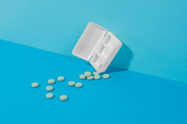 Pill container on blue surface with scattered pills.