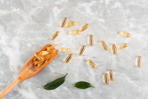 Fish oil capsules on a wooden spoon on a marble background.